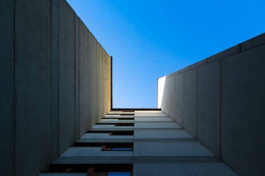 Minimalist architectural perspective of modern concrete building walls converging toward a bright blue sky