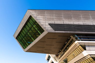 Viyana Üniversitesi Kütüphanesi 'nin modern mimarisi açık mavi gökyüzü altında dinamik camlı yapı içerir.