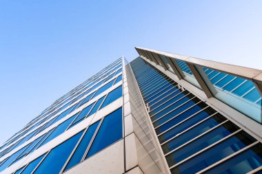 Açık mavi gökyüzüne karşı yansıtıcı metal cepheli ve geometrik çizgileri olan modern yüksek katlı konut kulesi