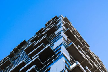 Modern residential building facade with geometric bay windows and reflective blue glass creating dynamic architectural texture
