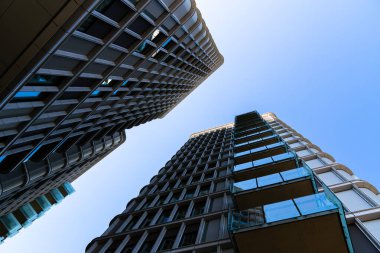 Açık mavi gökyüzüne karşı yansıtıcı metal cepheli ve geometrik çizgileri olan modern yüksek katlı konut kulesi