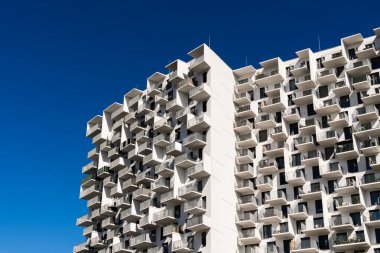 Modern residential architecture with repeating balconies and geometric facade under bright clear blue sky background
