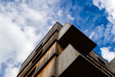 Parlak bulutlu mavi gökyüzüne karşı açısal beton balkonları ve geometrik tasarımı olan modern ahşap konut binası