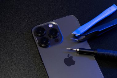 South Tyrol, Italy - Jan. 7. 2023: Repair tools on top of Apple iPhone Pro. Screwdriver and Tweezers on Smartphone for repair