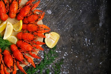 Pişmiş kırmızı nehir kerevitleri ahşap tabağın etrafında beton zemin, limon ve otlarla kaplı.