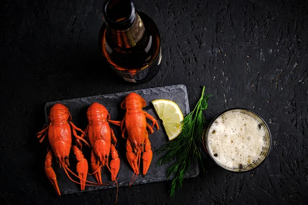 stock image Boiled river crayfish with lemon and dill on slate and bottle with glass of foam beer