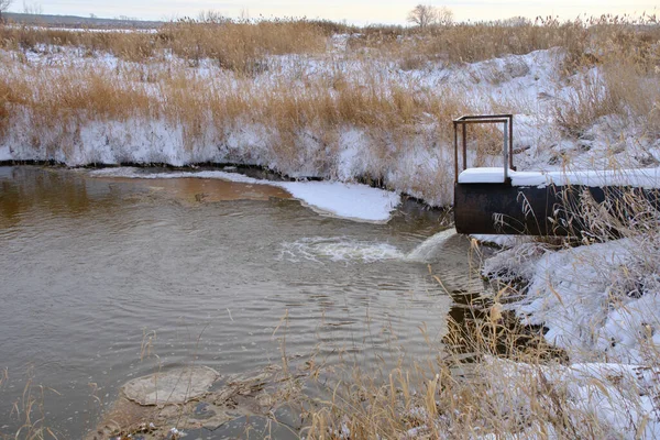 Sewage discharge from pipe into river in winter, river pollution and ecology