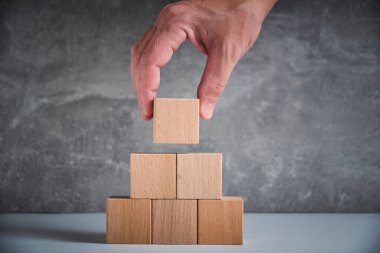 Laying out by hand a pyramid wooden cubes leading up.Concept growth and development