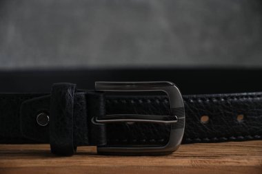 Men black leather belt with metal buckle wooden table and on gray wall background