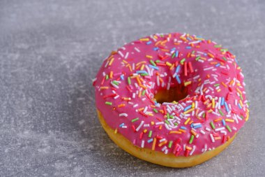Doughnut with pink icing and multicolored powdered sugar gray concrete background