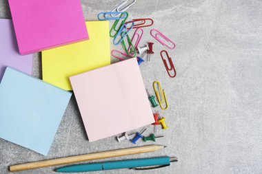 Bundles of multicolored stickers for written notes with chancellery on gray background