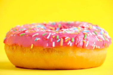 Donut with pink icing and multicolored sugar sprinkles.On yellow background,closeup