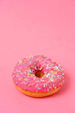 Donut with pink icing and multicolored sugar sprinkles.On pink background
