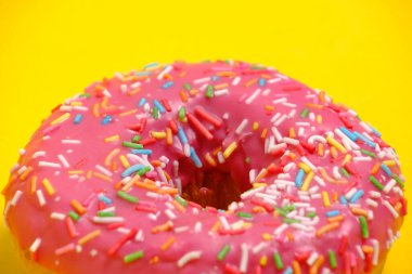 Donut with pink icing and multicolored sugar sprinkles.On yellow background,closeup