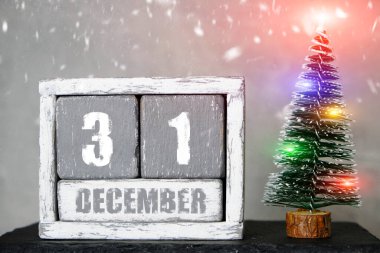 December 31 on wooden calendar background of Christmas tree with garlands and falling snow.Concept upcoming new year