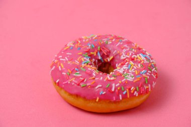Donut with pink icing and multicolored sugar sprinkles.On pink background