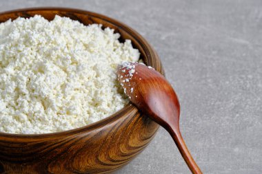 Delicious homemade cottage cheese in wooden cup gray background