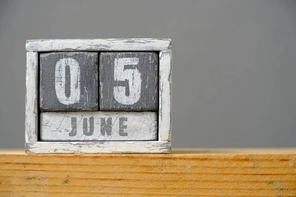 Calendar for June 05 made of wooden cubes standing on shelf on gray background.With an empty space for your text