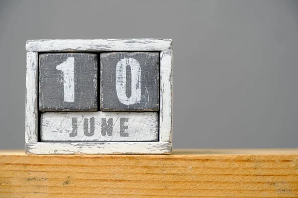 Calendar for June 10 made of wooden cubes standing on shelf on gray background.With an empty space for your text