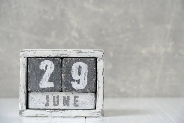 Calendar for June 29, made wooden cubes, against light concrete wall.With an empty space for your text
