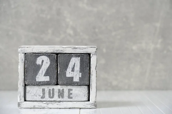 Calendar for June 24, made wooden cubes, against light concrete wall.With an empty space for your text