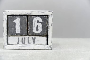 16 Temmuz takvimi, tahta küplerden yapılmış, gri arkaplan üzerinde. Metnin için boş bir boşluk var.