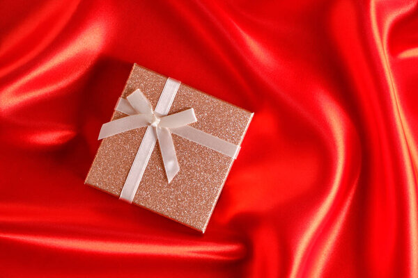 Brown gift box with a brown ribbon and bow on a red fabric, silk background