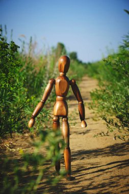 Ahşap manken yeşil bitkilerin arasında yol boyunca yürüyor.