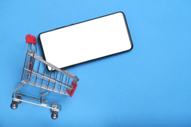 Alışveriş sepeti ve beyaz ekran mavi arka planlı akıllı telefon. Çevrimiçi alışveriş kavramı