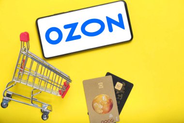 Kostanay, Kazakistan, 31 Ağustos 2023. OZON en büyük Rus çevrimiçi perakendecisi Yaban mersini logosu, alışveriş sepeti ve banka kartları içeren akıllı telefon. Çevrimiçi alışveriş kavramını ele alalım.