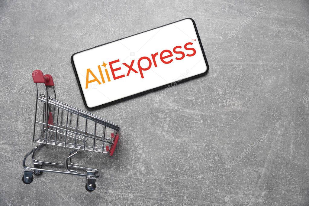 Kostanay, Kazakhstan, August 31, 2023. Smartphone with Aliexpress logo, shopping basket gray concrete background.Concept of online shopping