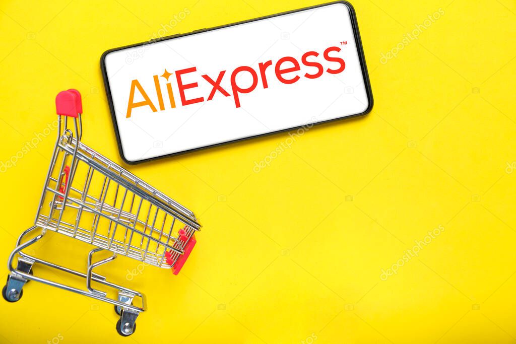 Kostanay, Kazakhstan, August 31, 2023. Smartphone with aliexpress logo,shopping basket yellow background.Concept online shopping