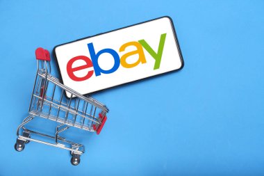 Kostanay, Kazakistan, 31 Ağustos 2023 ebay logolu akıllı telefon, alışveriş sepeti mavi arka plan. İnternet üzerinden alışveriş kavramı