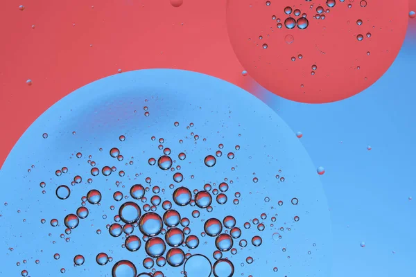 円の油滴が付いているマクロの写真水面 オイルバブルによる抽象的な青と赤の背景 — ストック写真