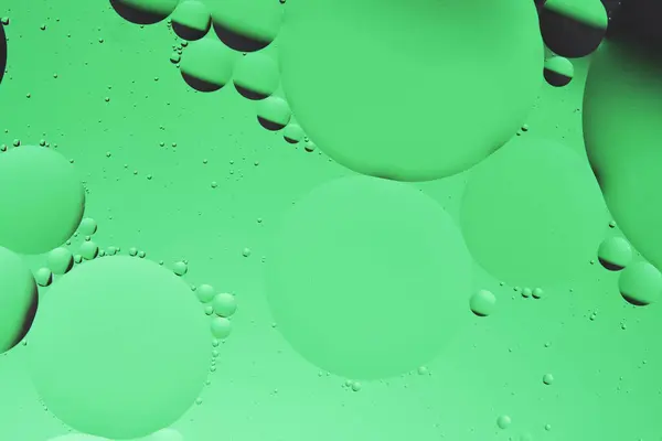Macro photo with circles oil droplets water surface. Abstract green background with oil bubbles