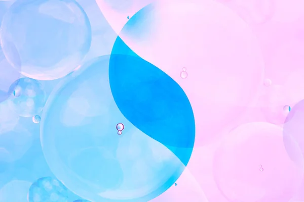 Macro photo with circles oil droplets water surface. Abstract blue and pink background with oil bubbles