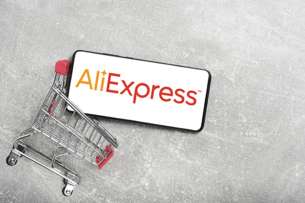 Kostanay, Kazakistan, 31 Ağustos 2023. Aliexpress logolu akıllı telefon, alışveriş sepeti gri beton arka plan. İnternetten alışveriş kavramı.
