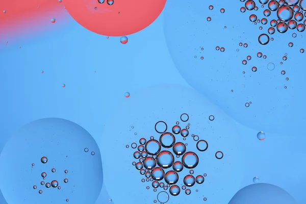 Macro photo with circles oil droplets water surface. Abstract blue and red background with oil bubbles