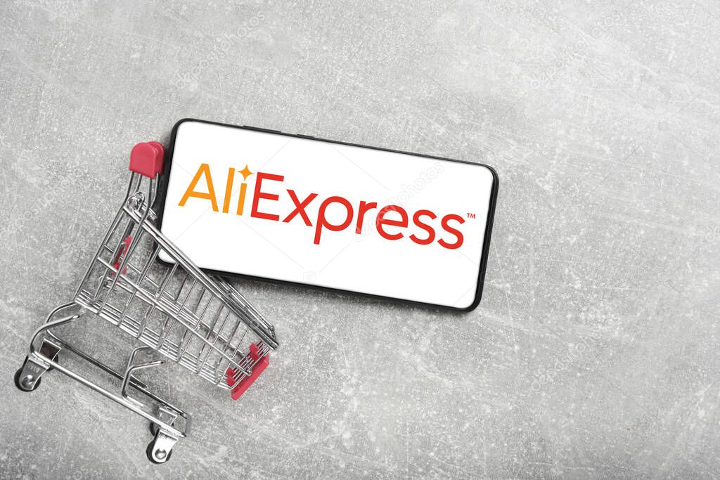 Kostanay, Kazakhstan, August 31, 2023. Smartphone with Aliexpress logo, shopping basket gray concrete background.Concept of online shopping