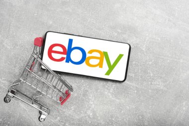Kostanay, Kazakistan, 31 Ağustos 2023. ebay logolu akıllı telefon, alışveriş sepeti gri beton arka plan. İnternetten alışveriş kavramı.