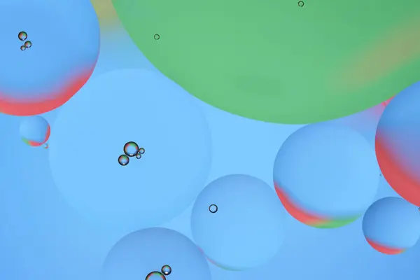 Macro photo with circles oil droplets water surface. Abstract blue, green and red background with oil bubbles