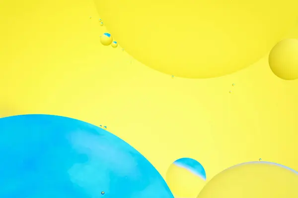 Macro photo with circles oil droplets water surface. Abstract blue and yellow background with oil bubbles