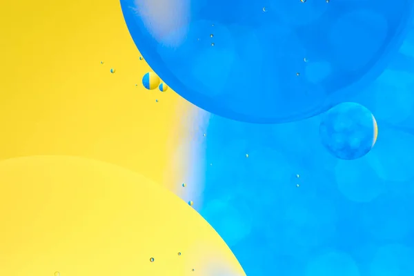 Macro photo with circles oil droplets water surface. Abstract blue and yellow background with oil bubbles