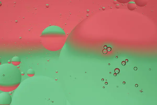 Macro photo with circles oil droplets water surface. Abstract green and red background with oil bubbles