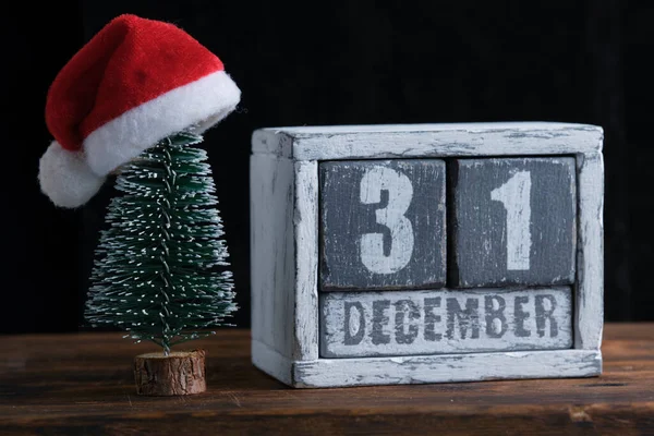 31 Aralık, Noel Baba şapkasıyla süslenmiş Noel ağacının yanında duran ahşap takvim üzerine