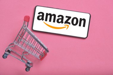 Kostanay, Kazakistan, 31 Ağustos 2023. Amazon logolu akıllı telefon, alışveriş sepeti pembe arka plan. İnternet üzerinden alışveriş kavramı..