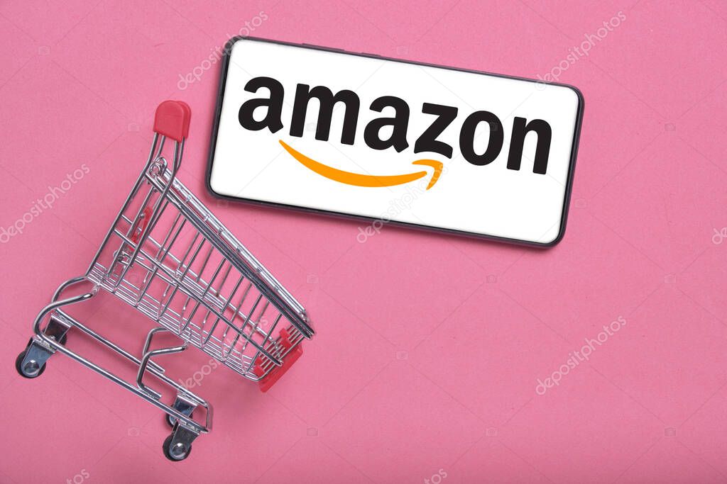 Kostanay, Kazakhstan, August 31, 2023.Smartphone with amazon logo,shopping basket pink background.Concept online shopping.