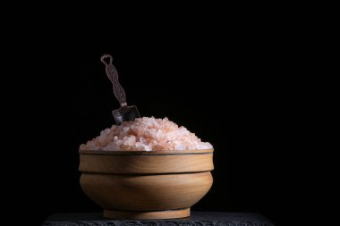Pembe tuz ve baharat kaşığıyla ahşap bardak, aydınlatılmış muhteşem siyah arka plan.