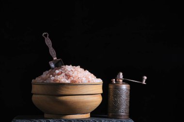 Pembe tuz, değirmen ve baharat kaşıklı ahşap bardak etkili bir şekilde siyah arka plan vurgulanır