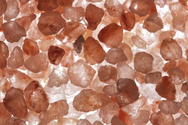 Aydınlatılmış pembe tuzun açık arkaplandaki makro görüntüsü hassas renklerde karmaşık kristal yapılar sergiliyor.